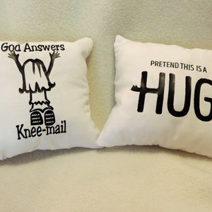 May include: Two white throw pillows with black text. One pillow says "Good Answers Knee-mail" with a cartoon drawing of a person with their arms raised. The other pillow says "Pretend this is a HUG" with arms on either side of the word hug.