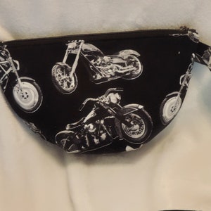 May include: Black fabric fanny pack with a zipper closure and a white print of motorcycles. The fanny pack has a long strap.