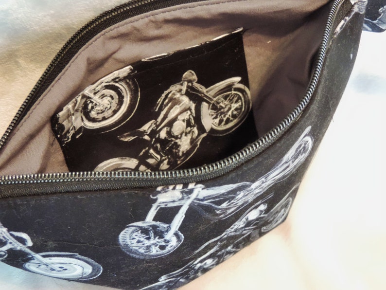 May include: Black zippered pouch with a gray lining. The pouch is decorated with a repeating pattern of white motorcycles. The lining has a pocket with a motorcycle graphic.