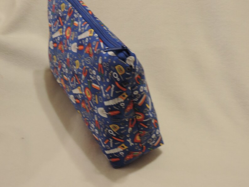 Puede incluir: Una bolsa azul con cremallera con un patr&oacute;n colorido de herramientas y ferreter&iacute;a. La bolsa est&aacute; hecha de tela y tiene un cierre de cremallera.