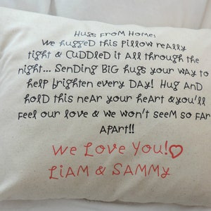 May include: A white pillow with black text that reads "Hugs from home: We hugged this pillow really tight & cuddled it all through the night... Sending big hugs your way to help brighten every day! Hug and hold this near your heart & you'll feel our love & we won't seem so far apart!! We love you!" with a red heart and "Liam & Sammy" in red text.