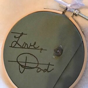 May include: A green fabric embroidery hoop with the words "Love Post" written in black ink.