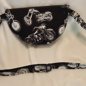 May include: Black fanny pack with a white adjustable strap. The fanny pack has a zipper closure and is decorated with a repeating pattern of white motorcycles.