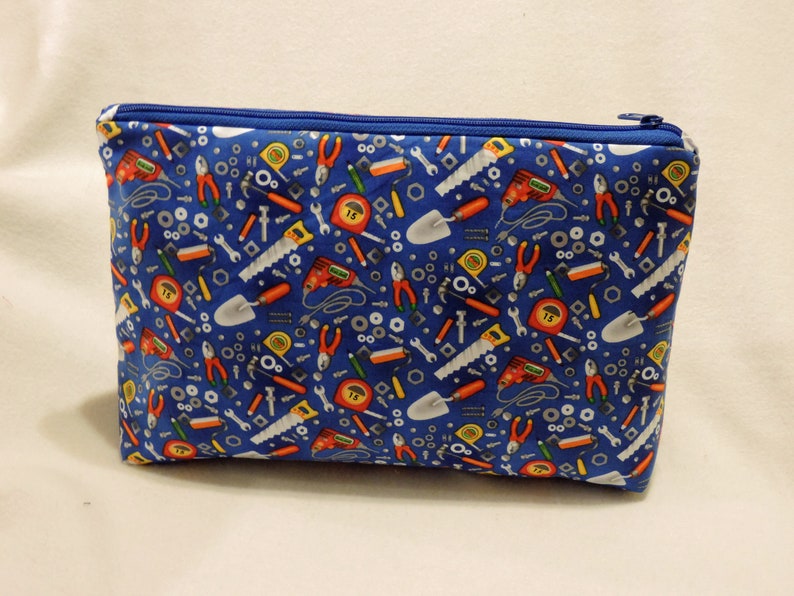 Puede incluir: Una bolsa azul con cremallera con un patr&oacute;n de herramientas, incluyendo llaves, destornilladores, martillos y cintas m&eacute;tricas.