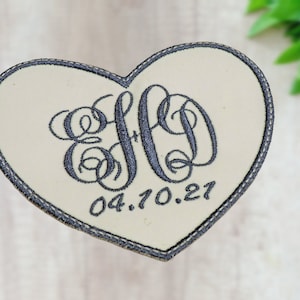 May include: A white heart-shaped patch with a black embroidered monogram and the date 04.10.21.