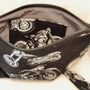 May include: A black zippered pouch with a gray lining and a black and white motorcycle print. The pouch has a zipper closure and a black strap.