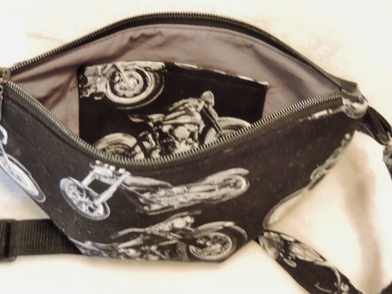 May include: A black zippered pouch with a gray lining and a black and white motorcycle print. The pouch has a zipper closure and a black strap.