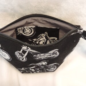 May include: Black zippered pouch with a gray lining. The exterior features a repeating pattern of white motorcycle silhouettes.