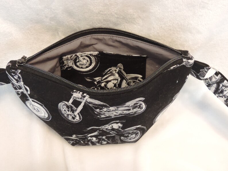 May include: Black zippered pouch with a gray lining. The exterior features a repeating pattern of white motorcycle silhouettes.