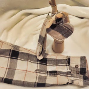 May include: A brown and white plaid fabric heart-shaped keychain with a silver key ring attached to a wooden hand.