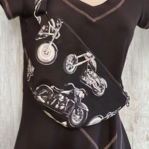 May include: A black fanny pack with a white motorcycle print. The pack has a long adjustable strap.