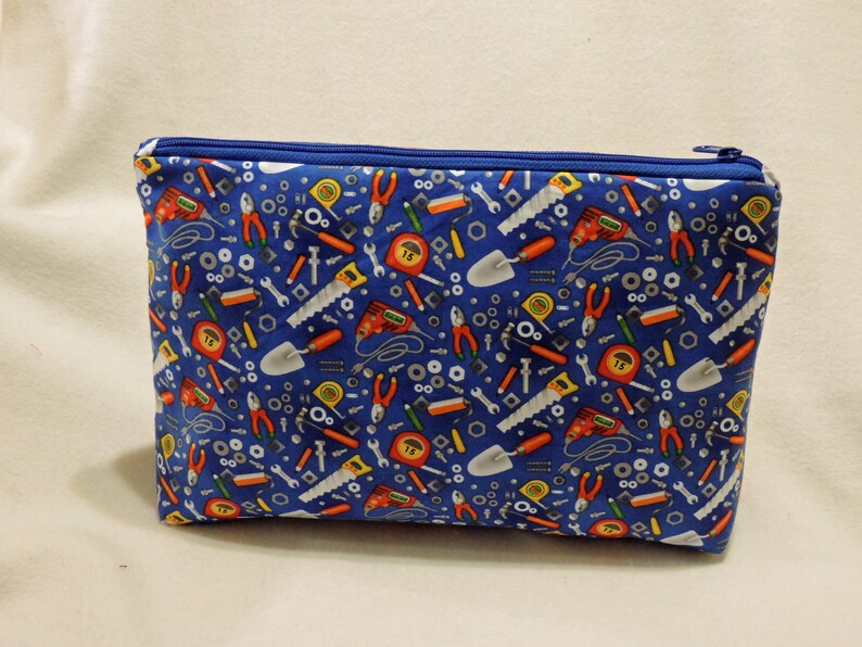 Puede incluir: Una bolsa azul con cremallera con un patr&oacute;n de varias herramientas, incluyendo llaves, destornilladores, martillos, alicates y cintas m&eacute;tricas.