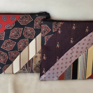 May include: Two rectangular zippered pouches constructed from repurposed neckties. The left pouch features diagonal panels of red, navy blue, and beige with paisley and geometric patterns. The right pouch displays diagonal stripes of purple, yellow, and grey.