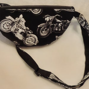 May include: Black fanny pack with a white motorcycle print. The pack has a zipper closure and an adjustable strap.