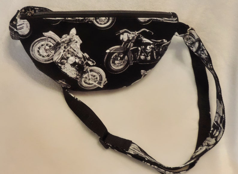 May include: Black fanny pack with a white motorcycle print. The pack has a zipper closure and an adjustable strap.