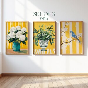 May include: A set of 3 prints featuring yellow and white striped backgrounds. The first print shows white hydrangea flowers in a teal vase. The second displays green foliage in a patterned urn. The third depicts a blue bird on a flowering branch.
