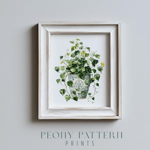 Puede incluir: Una impresión enmarcada de una planta en maceta. La planta tiene hojas verdes en forma de corazón en una maceta con estampado azul y blanco. El marco blanco tiene un acabado envejecido. El texto "PEONY PATTERN PRINTS" está en la parte inferior.