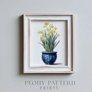 May include: A framed watercolor print featuring a potted daffodil plant. The plant has bright yellow flowers and green leaves, set in a blue ceramic pot. The frame is white with a distressed finish. The text "PEONY PATTERN PRINTS" is at the bottom.