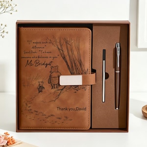 May include: A tan leather-like journal featuring an engraved Winnie the Pooh illustration, the text "It makes such a difference" Said Pooh "To have someone who believes in you", "Ms. Bridget", and "Thank you, David", paired with a matching pen in a box.