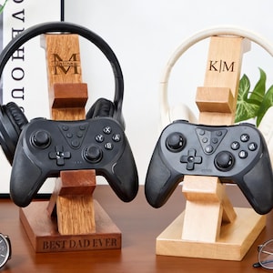 May include: Two wooden headphone stands with game controllers. One stand holds black headphones and the other holds white headphones. The stands are engraved with initials and the text "BEST DAD EVER".