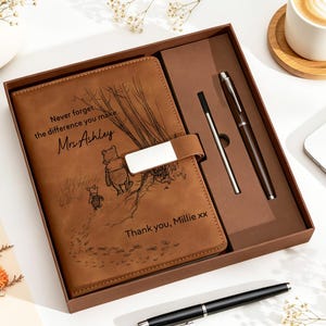 May include: A brown leather-look notebook gift set featuring a Winnie the Pooh and Piglet illustration with the text "Never forget the difference you make Mrs. Ashley" and "Thank you, Millie xx". The set includes a matching pen and a refill.