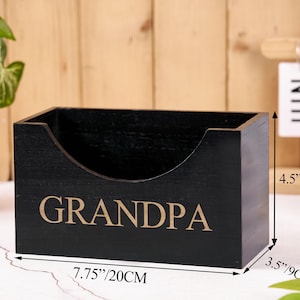 Puede incluir: Una caja de madera negra con la palabra "GRANDPA" en letras doradas. La caja mide 20 cm de largo, 9 cm de ancho y 11,5 cm de alto. La caja tiene un recorte curvo en un lado.