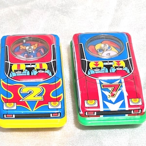 May include: Two vintage toy race cars. One is red, blue, and yellow with the number 2. The other is red, blue, and green with the number 7. Each car has a clear bubble on top with a driver inside.