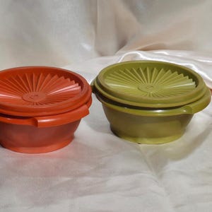 May include: Four vintage plastic bowls in shades of brown, orange, olive green, and yellow. Each bowl has a matching lid with a sunburst design. The bowls are arranged in a row, showcasing their different colors and shapes.