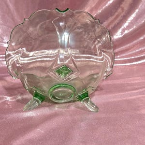 May include: A clear glass bowl with a scalloped rim and three green-tipped feet. The bowl has a decorative green accent in the center and on the feet. The bowl is likely vintage and suitable for serving.
