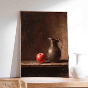 May include: A framed still life painting featuring a red apple and a dark metallic pitcher. The artwork has a warm, brown color palette and is displayed on a wooden shelf. A white vase is to the right of the painting.