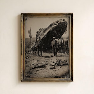 May include: A framed black and white photograph depicting two individuals in hats standing in a desert landscape near a large, metallic, circular wreckage. A horse stands nearby, and a tall saguaro cactus is visible in the background.