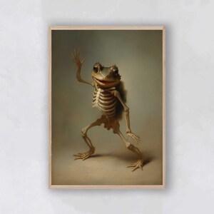 May include: A framed print featuring a whimsical illustration of a frog skeleton. The frog is depicted in a standing pose, with one arm raised. The artwork has a vintage aesthetic, with a neutral background and a wooden frame.