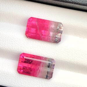 May include: Two rectangular gemstones, predominantly pink with a clear, pale transition. The gems are faceted, revealing their internal structure. They are displayed against a white background.