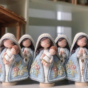 May include: Five handmade crochet dolls, each representing a religious figure holding a baby. The dolls are dressed in light blue and white robes, adorned with floral and pearl details. Each has a white head covering and closed eyes.