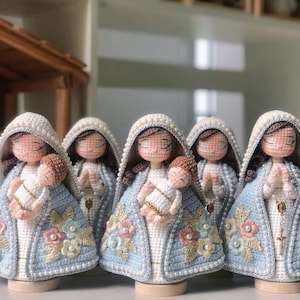 May include: Five handmade crochet dolls, each representing a religious figure holding a baby. The dolls are dressed in light blue and white robes, adorned with floral and pearl details. Each has a white head covering and closed eyes.
