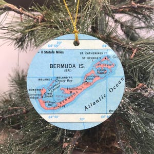 May include: Round Christmas ornament featuring a map of Bermuda. The map is in shades of blue, with red accents highlighting the islands and place names like Hamilton and St. George's. The ornament has a gold string for hanging.