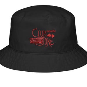 May include: Black bucket hat with red embroidered text that reads "Club Juke". The hat features a wide brim and a rounded crown. The text includes a musical instrument design and playing card symbols.
