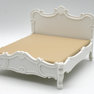 Puede incluir: Una cama de muñeca blanca y ornamentada con un colchón beige. El marco de la cama presenta tallas detalladas y un cabecero decorativo. La cama está diseñada en un estilo clásico y elegante, perfecta para miniaturas.