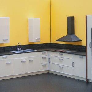 Könnte beinhalten: Eine Miniaturküche mit weißen Schränken, einer schwarzen Arbeitsplatte und einem schwarzen Kühlschrank. Die Küche verfügt über einen Einbaubackofen, eine Dunstabzugshaube und ein Edelstahlbecken. Die Wände sind gelb gestrichen.
