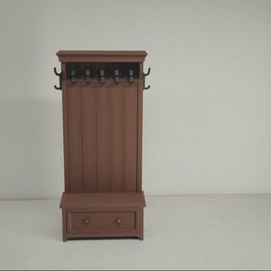 以下が含まれることがあります： ベンチ、引き出し、コートフックが付いた茶色の木製ホールツリー。ホールツリーは垂直パネルのデザインと長方形の形状をしています。コートフックは黒です。ベンチには2つのノブが付いた引き出しがあります。