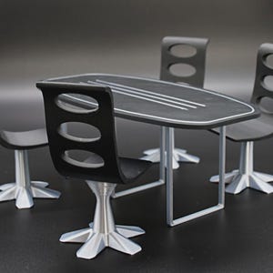 May include: A miniature black dining table with four matching chairs. The table has a black surface with white trim and three white lines. The chairs have a unique design with three oval cutouts in the back and silver-colored bases.