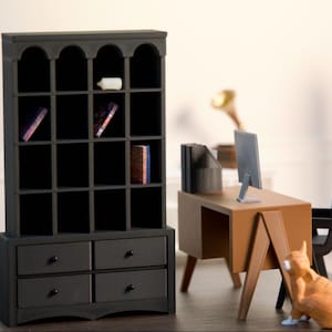 Może przedstawiać: Miniaturowy czarny regał z łukowatym blatem, szufladami i półkami. Obecne jest również małe biurko z monitorem komputerowym, czarnym krzesłem i gramofonem. Pomarańczowy kot siedzi w pobliżu biurka.