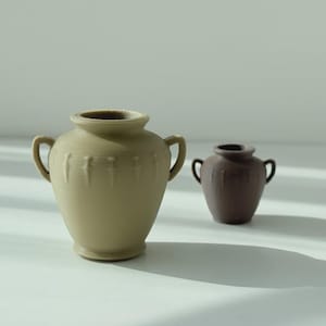 May include: Two ceramic vases. The larger vase is light beige with two handles and vertical grooves. The smaller vase is dark brown with two handles. Both vases have a classic urn shape and sit on a white surface.