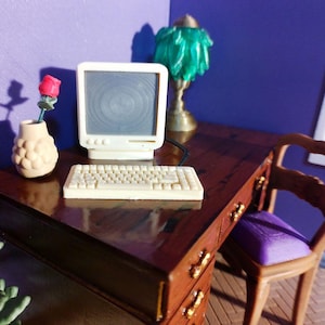 May include: Miniature office scene with a computer, keyboard, and desk. The desk is dark wood with gold drawer pulls. A small vase holds a red rose. A green lamp and a purple chair complete the scene. The computer monitor is white.