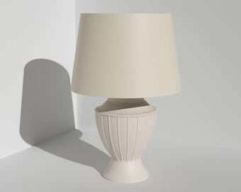 Könnte beinhalten: Eine cremefarbene Tischlampe mit einem konischen Lampenschirm. Der Sockel hat ein geripptes Design und einen abgerundeten Sockel. Die Lampe wirft einen Schatten auf die weiße Oberfläche. Wohnkultur.
