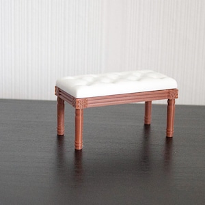 Puede incluir: Banqueta en miniatura con un cojín blanco acolchado y un marco de madera marrón. Las patas y el marco tienen tallas decorativas. Esta pequeña banqueta es una pieza decorativa.