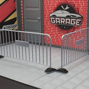 May include: A model garage scene featuring a metal barrier. The scene includes a red brick wall with a "GARAGE" sign and a "WORKSHOP" sign. The barrier is grey and has a rectangular sign attached to it.