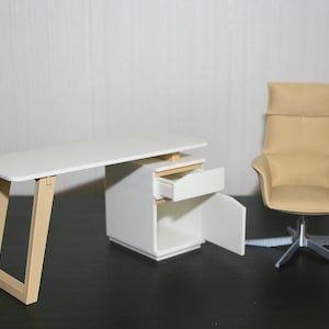 Puede incluir: Escritorio blanco en miniatura con una pata de color madera clara y un armario a juego con un cajón abierto. Una silla de oficina beige con base plateada está a la derecha. El conjunto está diseñado para una casa de muñecas o un entorno en miniatura.