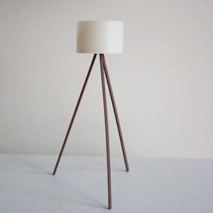 May include: A contemporary floor lamp featuring a cylindrical white lampshade. The lamp has a tripod base constructed from dark brown metal. The design is minimalist, suitable for home decor.