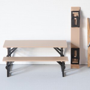May include: A miniature picnic table with a tan tabletop and bench, supported by black legs. A matching tan and black object and a large wooden clothespin are also present, all against a white background.